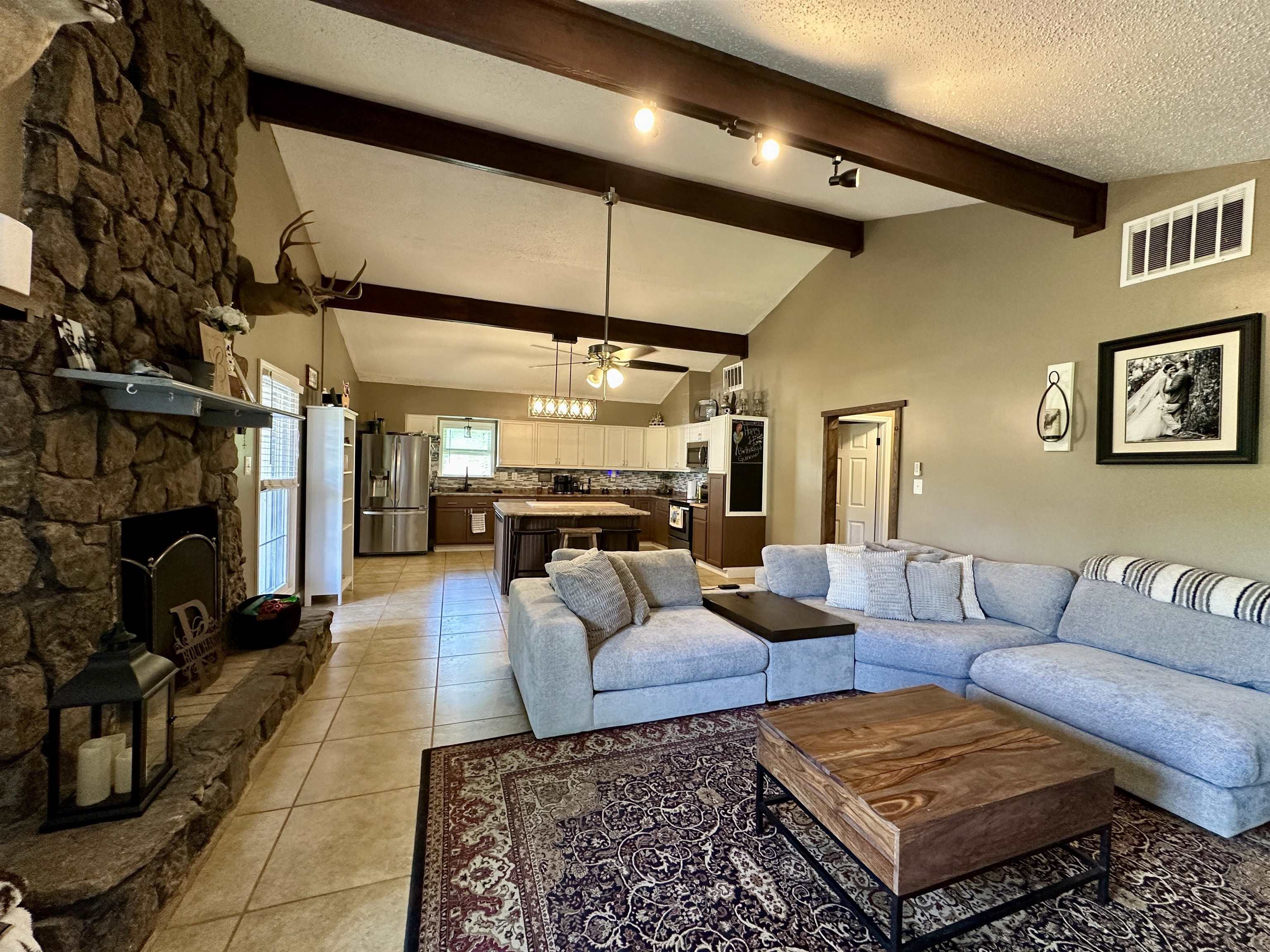 1230 Joann Road Somerville, TN 38068 - Photo 4 of 29 Spacious living area featuring a vaulted ceiling with exposed wood beams, a prominent stone fireplace, and light-toned tile flooring