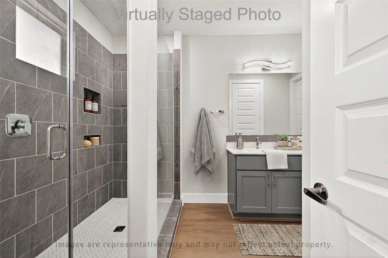 10719 Mason Road, Unit 39 Richmond, TX 77406 - Photo 22 of 50 Virtual Staging - This is a modern bathroom featuring a glass-enclosed walk-in shower with grey tile, a sleek grey vanity, and light wood-style flooring