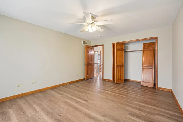 a view of an empty room with wooden floor and a ceiling fan