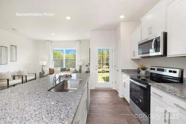 a kitchen with stainless steel appliances granite countertop a stove top oven a sink dishwasher a dining table and chairs with wooden floor