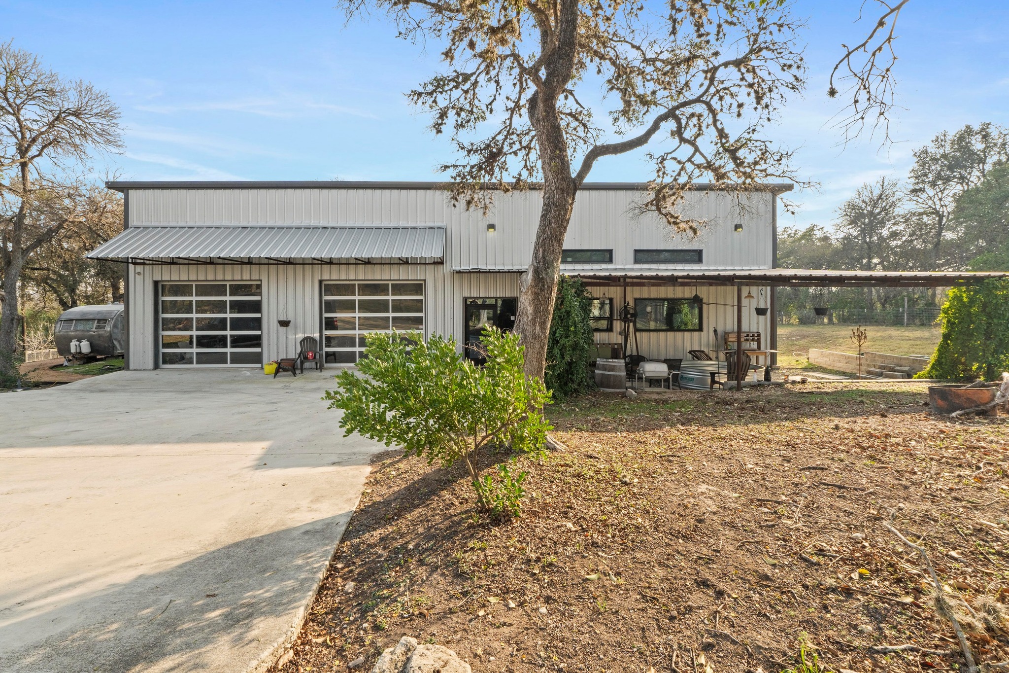 12302 Bethel Church Road Manchaca, TX 78652 - Photo 3 of 35 View of front facade featuring driveway, a garage, a metal roof, a patio area, and board and batten siding