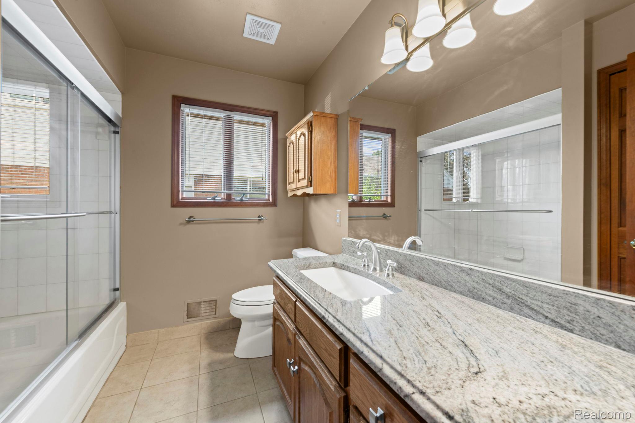 21580 Georgetown Road Trenton, MI 48183 - Photo 22 of 36 Bathroom featuring a generously sized vanity with a light-toned countertop and dual sinks, a large wall-mounted mirror, a tub/shower combination with sliding glass doors, two windows, and tile flooring