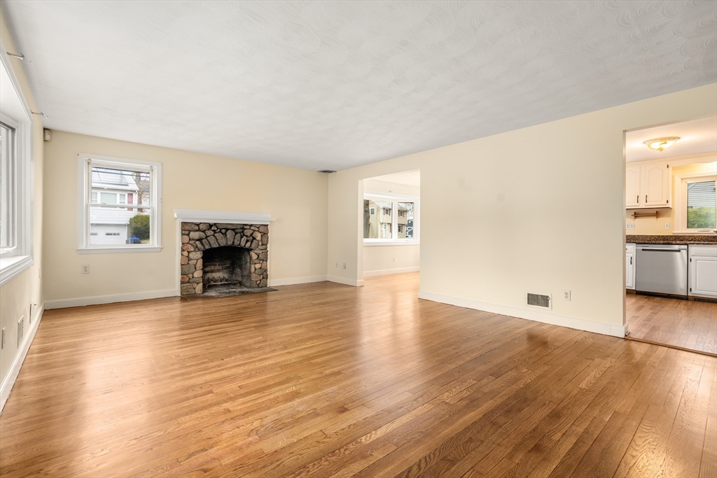 125 Lyman Road Milton, MA 02186 - Photo 5 of 25 an empty room with wooden floor a fireplace and windows