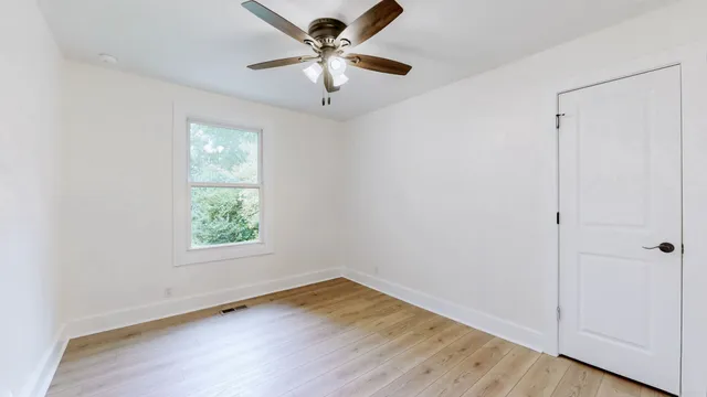 an empty room with wooden floor ceiling fan and windows