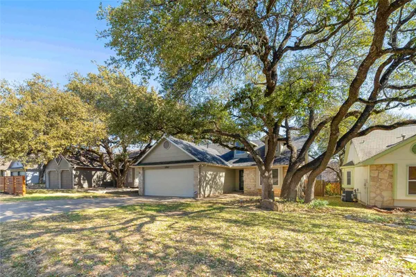 a yellow house in middle of a yard with large trees