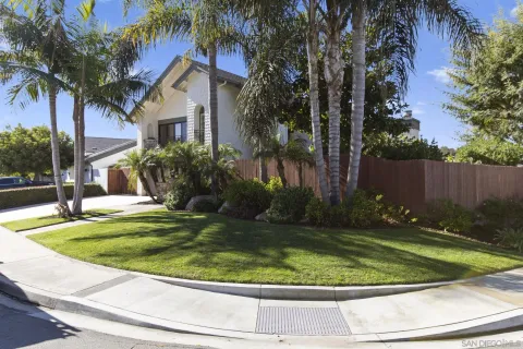a view of a white house with a yard plants and palm trees