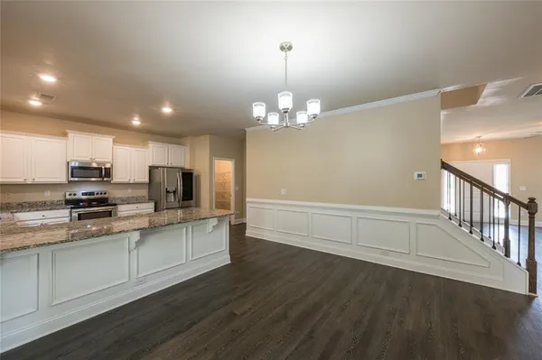 a kitchen with stainless steel appliances a microwave a stove a sink dishwasher a refrigerator and white cabinets with wooden floor