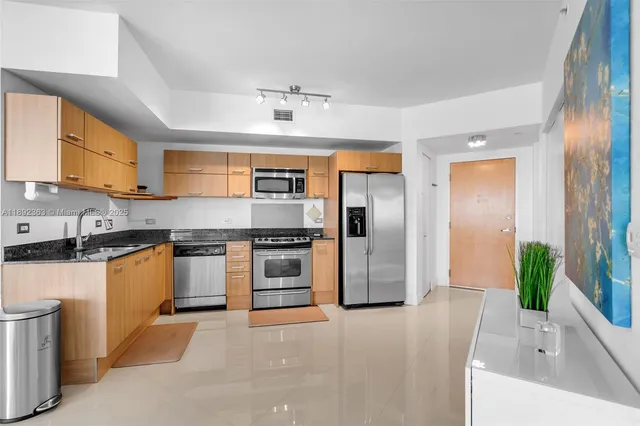 a large kitchen with stainless steel appliances kitchen island granite countertop a refrigerator a sink a stove a washer and dryer with wooden floor