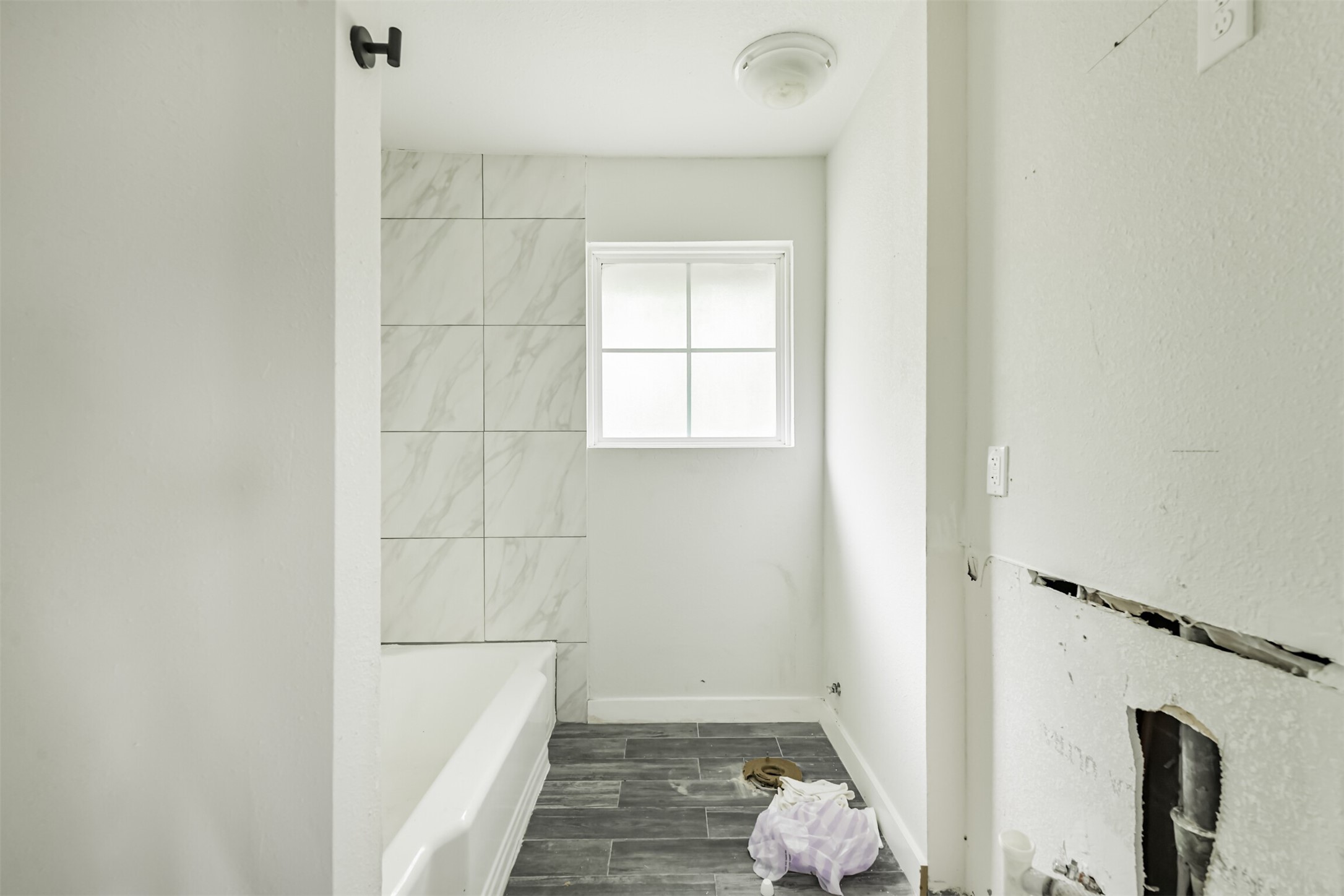 209 Leago Street Houston, TX 77022 - Photo 16 of 24 This photo shows a bathroom under renovation, featuring a tiled shower area with a bathtub, gray floor tiles, and a window providing natural light. Fixtures and fittings are yet to be installed.