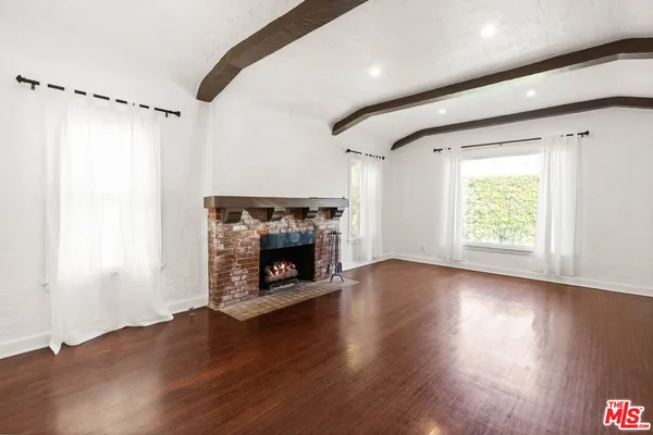 a view of an empty room with wooden floor fireplace and a window
