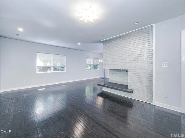 an empty room with wooden floor fireplace and windows