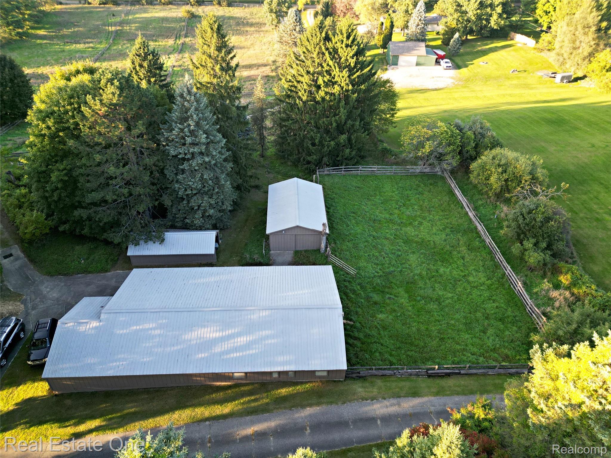 895 Rowe Road Milford, MI 48380 - Photo 18 of 50 Expansive property featuring a large outbuilding with a metal roof, a secondary outbuilding, a fenced grassy enclosure, and mature evergreen trees