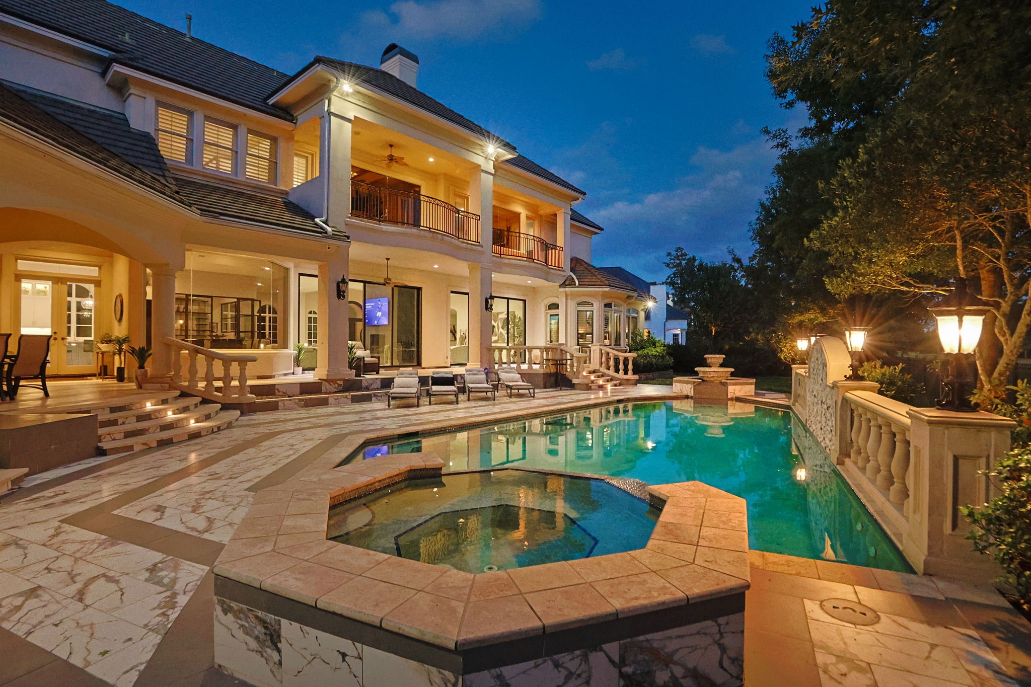 39 Maymont Way Spring, TX 77382 - Photo 43 of 50 This luxurious home features a stunning two-story exterior with elegant lighting, a spacious balcony, and a beautifully designed pool area complete with a spa and marble accents, perfect for entertaining and relaxation.