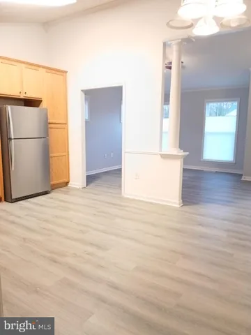 a view of empty room with wooden floor and kitchen