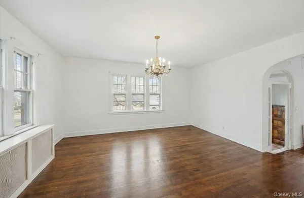 an empty room with wooden floor chandelier and windows