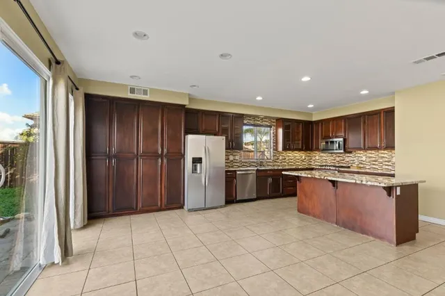 a large kitchen with stainless steel appliances kitchen island granite countertop a refrigerator and a sink