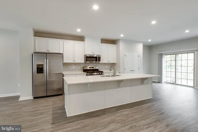 a kitchen with stainless steel appliances granite countertop a stove a sink a refrigerator and white cabinets with wooden floor