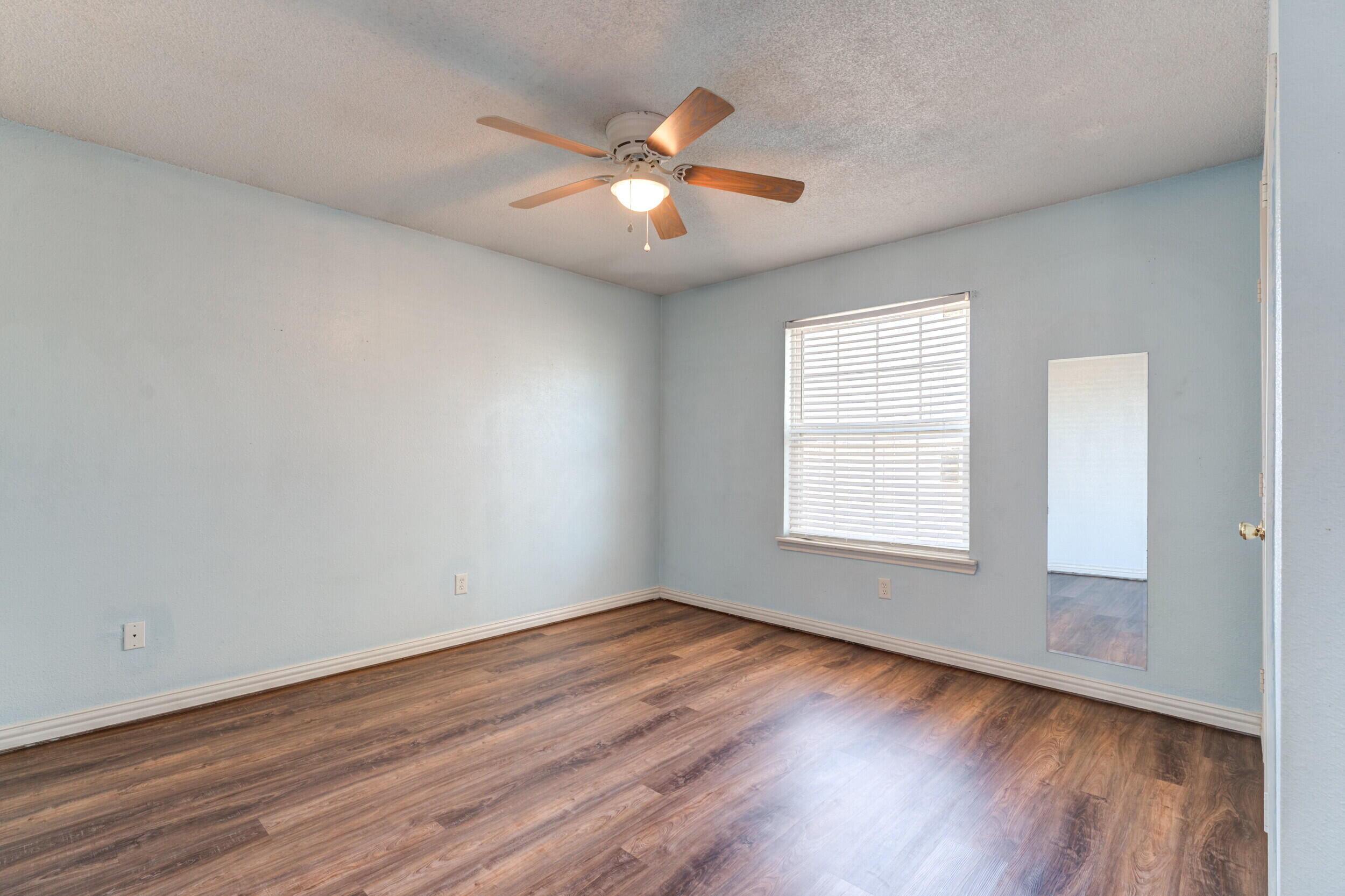 6325 14th Street Lubbock, TX 79416 - Photo 19 of 28 an empty room with wooden floor chandelier fan and windows