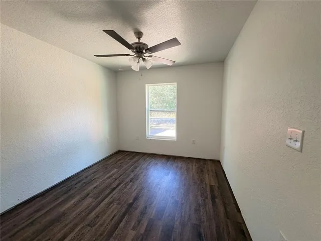 an empty room with wooden floor fan and windows