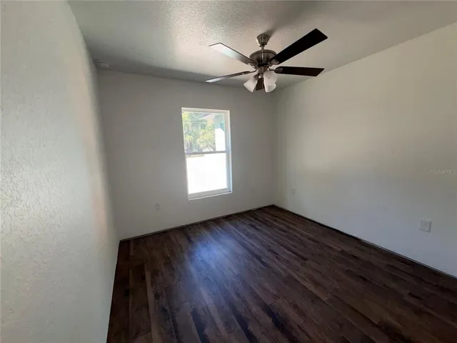 an empty room with wooden floor fan and windows