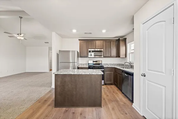 a kitchen with stainless steel appliances granite countertop a refrigerator a sink dishwasher a stove and white countertops with wooden floor