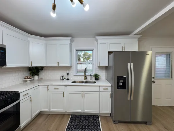 a kitchen with a sink dishwasher a refrigerator and white cabinets with wooden floor