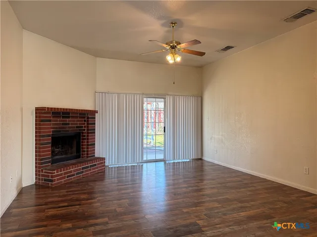 a view of an empty room with wooden floor fireplace and a window
