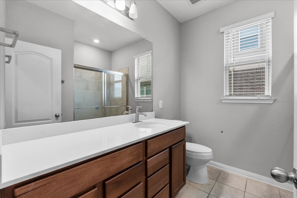 2320 Rosemary Street Rosenberg, TX 77469 - Photo 33 of 40 This is a modern bathroom featuring a large mirror, a double-sink vanity with ample storage, tile flooring, and a glass-enclosed shower. Natural light flows in through a window with blinds.