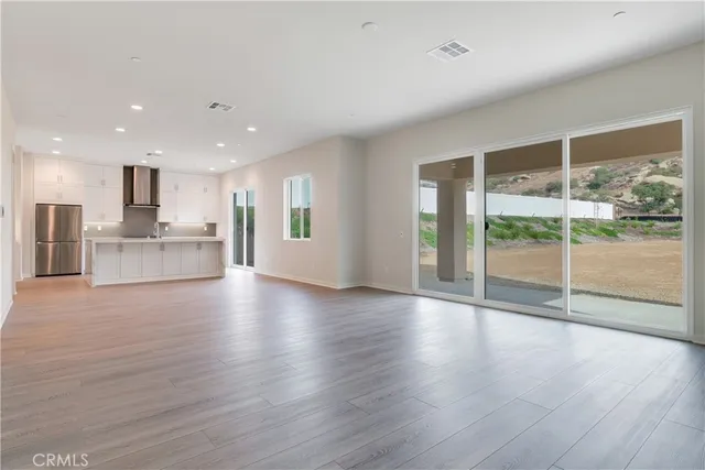 a view of an empty room with wooden floor and a kitchen