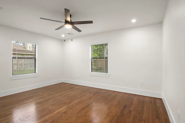 an empty room with wooden floor ceiling fan and windows
