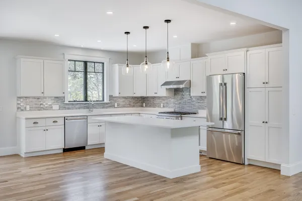 a kitchen with stainless steel appliances granite countertop a refrigerator a sink dishwasher a stove and white cabinets with wooden floor