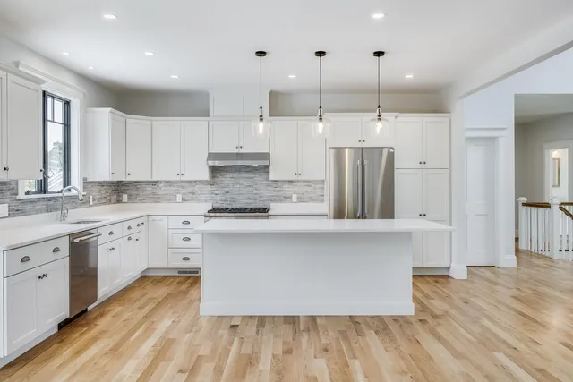 a kitchen with stainless steel appliances granite countertop a stove a sink dishwasher and white cabinets with wooden floor