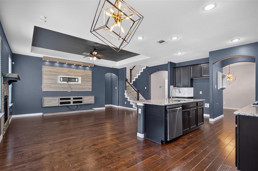 2066 Avondown Road Forney, TX 75126 - Photo 13 of 33 Open-concept living area featuring wood-finish flooring, a contemporary kitchen island with a stainless steel dishwasher, dark cabinetry, and granite countertops