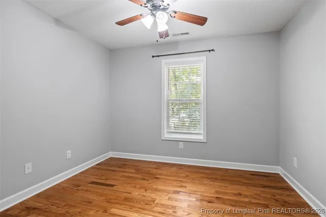 an empty room with wooden floor chandelier fan and windows