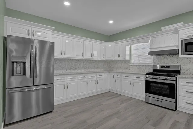 a kitchen with stainless steel appliances granite countertop a refrigerator a stove a sink and white cabinets