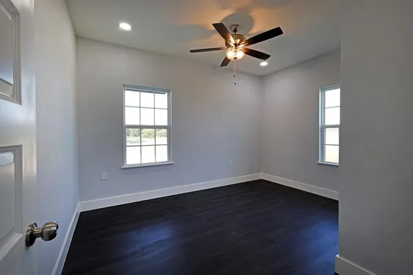 an empty room with wooden floor fan and windows