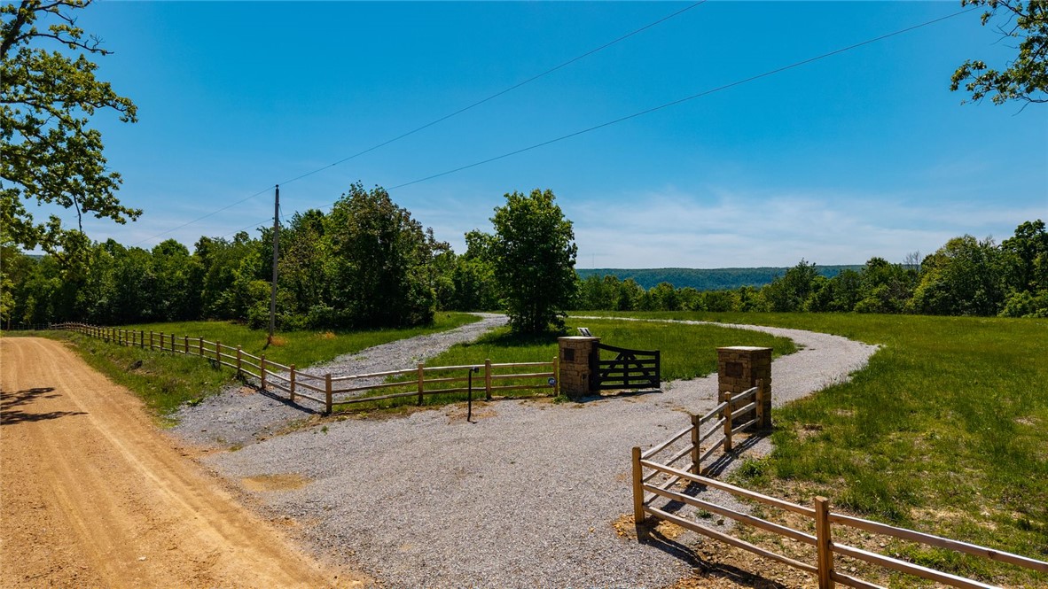 425 Barnhardt Road Timbo, AR 72680 - Photo 2 of 60 Gravel driveway leading to a gated entrance with stone pillars, featuring a wooden fence and expansive green fields with distant tree lines