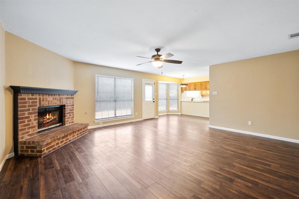 7517 Point Reyes Drive Fort Worth, TX 76137 - Photo 9 of 30 Spacious living area featuring wood-finish flooring, a brick fireplace with a dark mantel, and a ceiling fan with light fixture