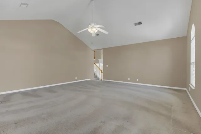 an empty room with a chandelier fan and windows