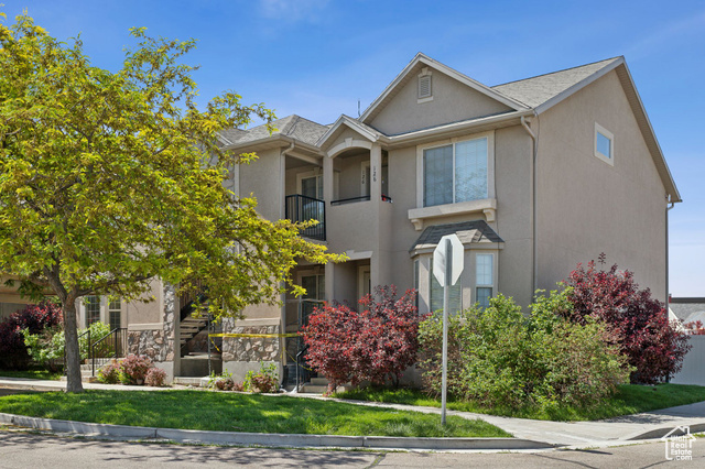 Multi unit property featuring a balcony, stucco siding, and a front lawn