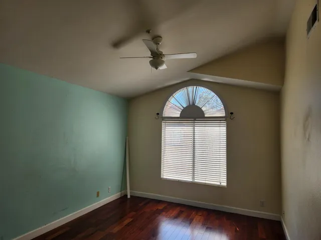 an empty room with wooden floor fan and windows