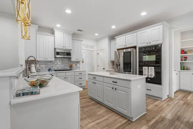 a kitchen with sink stove and white cabinets with wooden floor