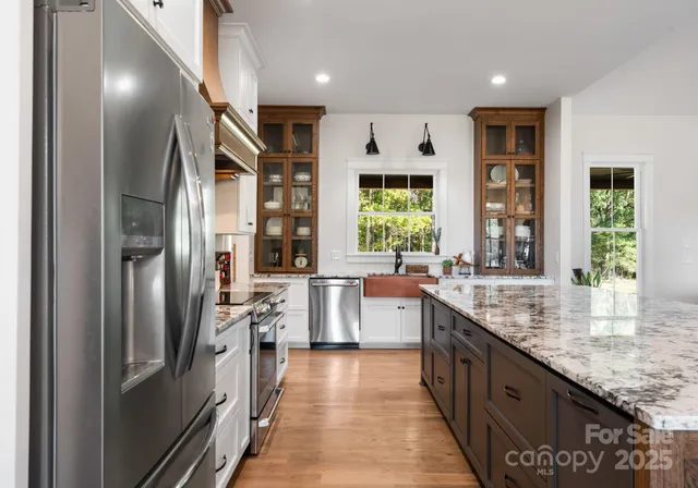 a kitchen with stainless steel appliances granite countertop a refrigerator a sink dishwasher a stove and a dining table with wooden floor