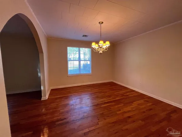 an empty room with wooden floor chandelier and windows