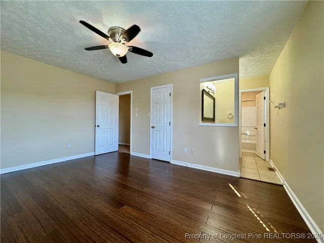 a view of an empty room with wooden floor and a ceiling fan