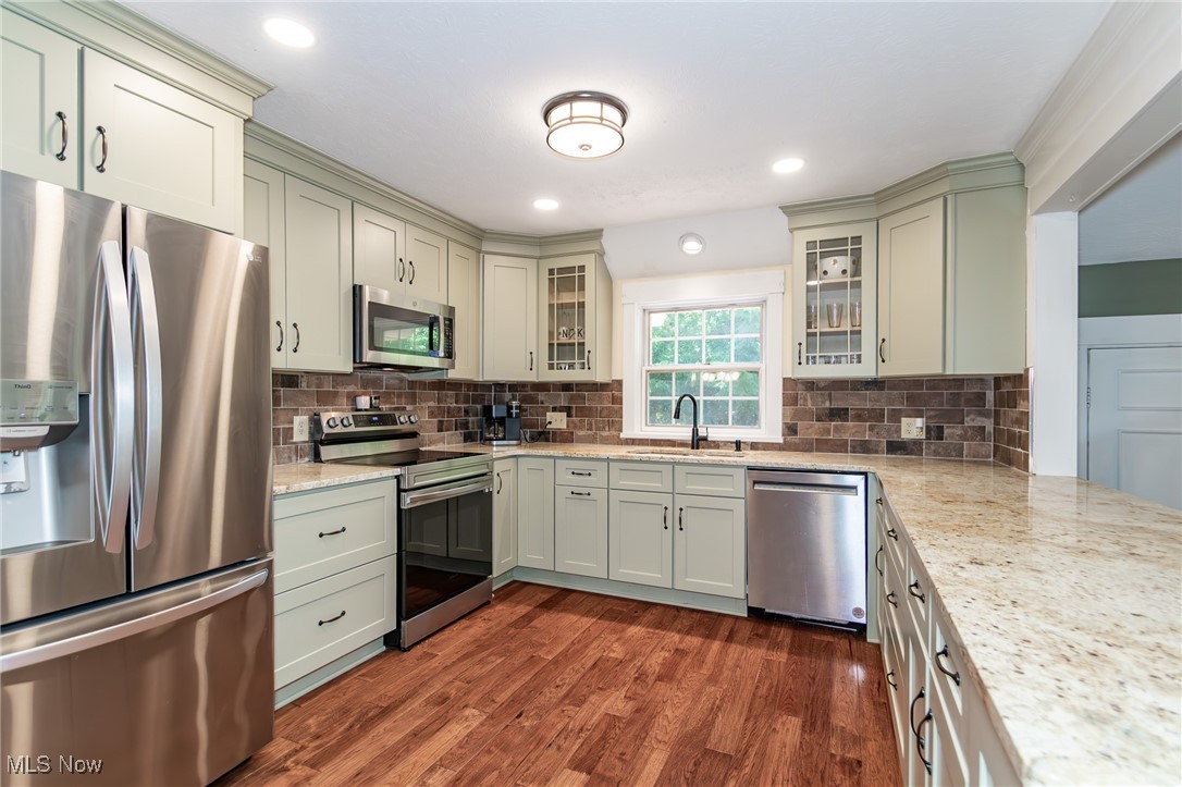 7806 Fairidge Road Willoughby, OH 44094 - Photo 16 of 41 Kitchen with appliances with stainless steel finishes, decorative backsplash, light stone countertops, glass insert cabinets, and dark wood-style flooring