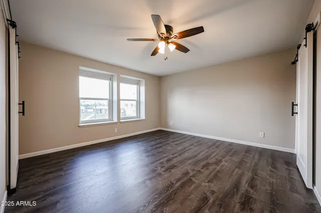 an empty room with wooden floor fan and windows