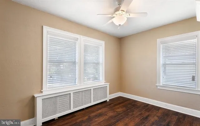 an empty room with wooden floor fan and windows