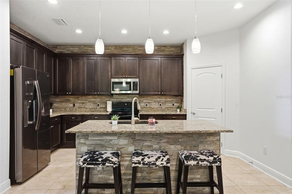 12417 Coralbean Court New Port Richey, FL 34654 - Photo 12 of 64 a kitchen with kitchen island granite countertop a table chairs microwave and refrigerator