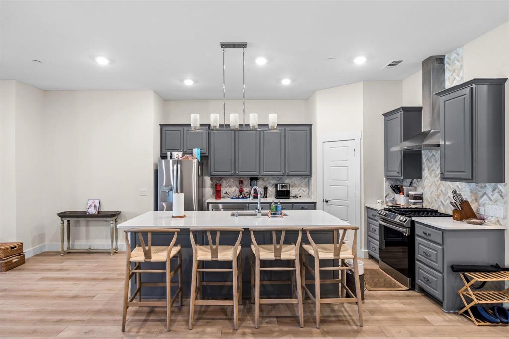 3781 Rochelle Court Prosper, TX 75078 - Photo 4 of 30 Kitchen with gray cabinetry, stainless steel appliances, light wood finished floors, a center island with sink, and decorative light fixtures